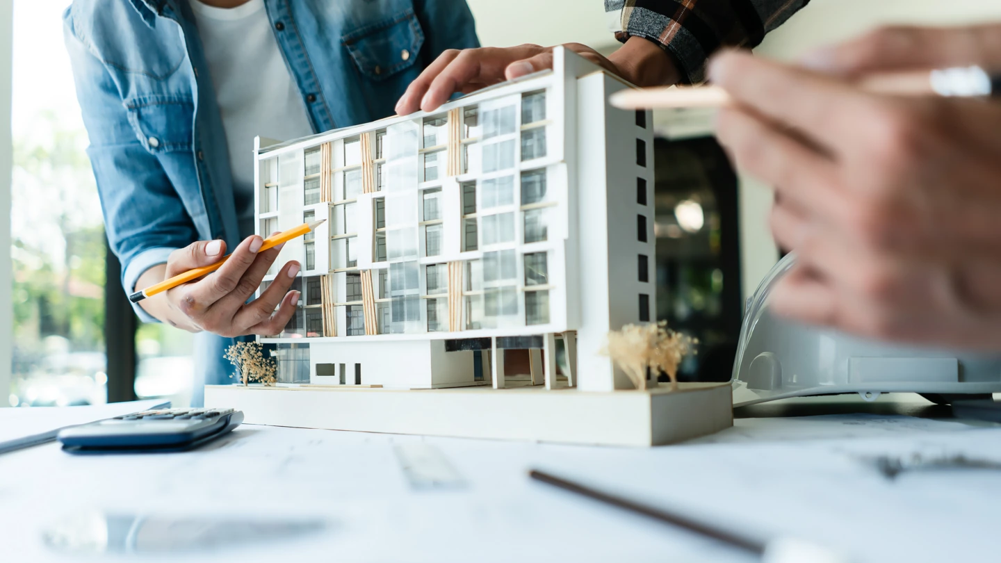 Builders reviewing an architectural model with blueprints